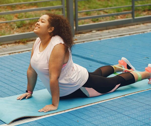 Smiling woman stretching gently on a yoga mat outdoors in a park.
